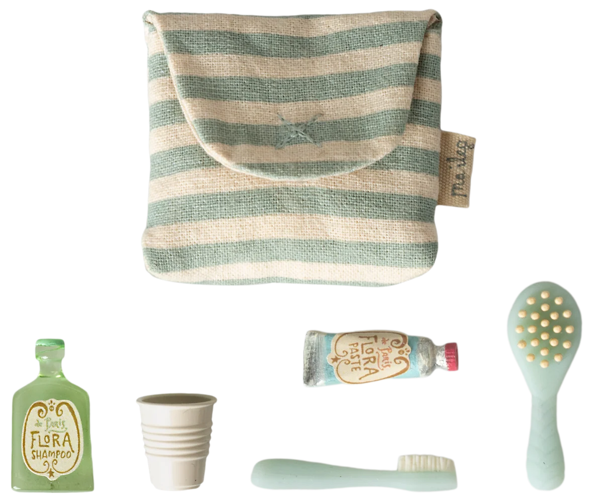 A set of travel-sized toiletry accessories on a white background, including a striped fabric pouch, a mint green toothbrush, a mint green hairbrush, a small mint green bottle labeled Flora Botánica, a small cup, and a tube of toothpaste.