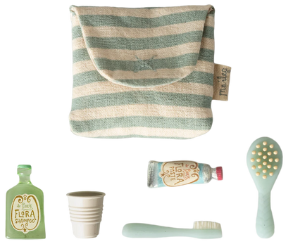 A set of travel-sized toiletry accessories on a white background, including a striped fabric pouch, a mint green toothbrush, a mint green hairbrush, a small mint green bottle labeled Flora Botánica, a small cup, and a tube of toothpaste.