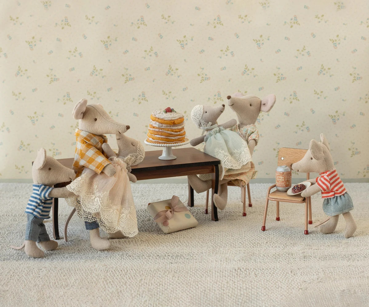 Toy mice gathered around a table with a cake in a decorative setting.
