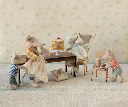 Toy mice gathered around a table with a cake in a decorative setting.