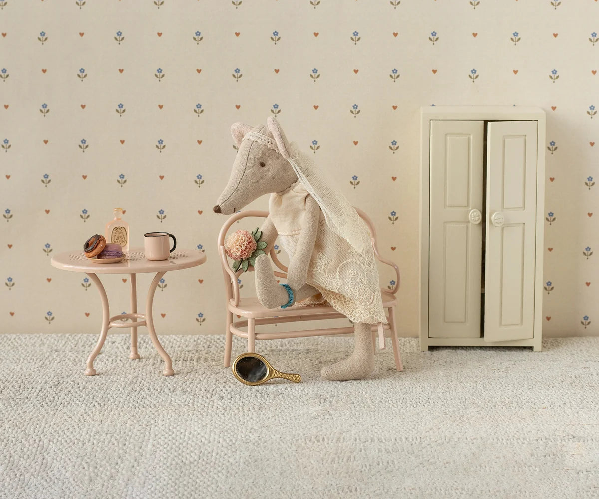 Stuffed animal in a room with a small table, chair, and cabinet against a patterned wall.