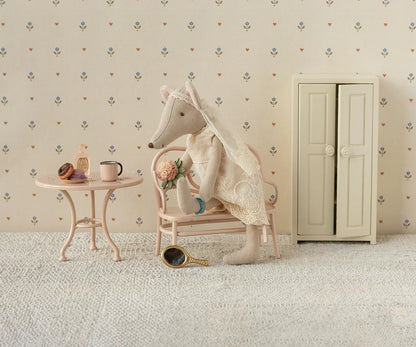 Stuffed animal in a room with a small table, chair, and cabinet against a patterned wall.