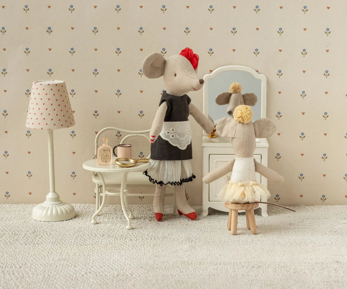Two toy mice in a room with a lamp, table, and mirror.