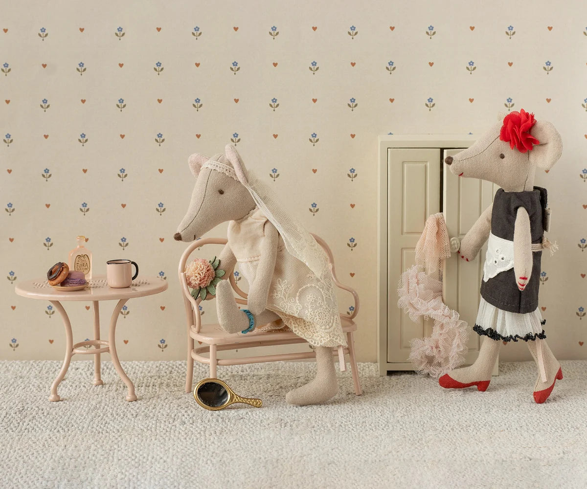Two plush toys, one resembling a mouse and the other a cat, in a room with floral wallpaper.
