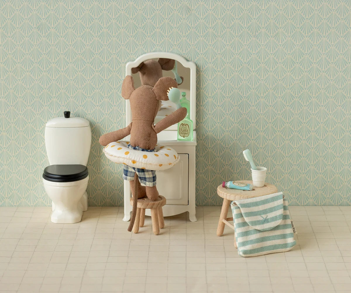 Stuffed teddy bear in a bathtub with bathroom items and wallpaper.