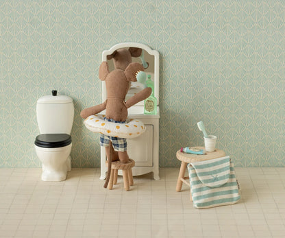 Stuffed teddy bear in a bathtub with bathroom items and wallpaper.