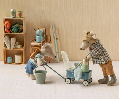Two plush animal figurines styled as a father and daughter pushing a blue stroller in a miniature room scene with a wooden shelf and cozy accessories.