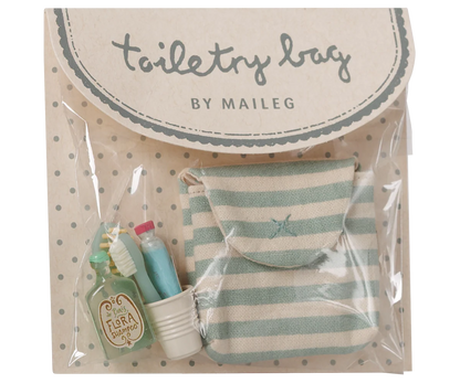 Toiletry bag set by Maileg in clear plastic packaging with a beige polka-dot backing card. The set includes a small striped mint green and cream pouch, a miniature green toiletry bottle labeled 'Tirra Loci', a small white cup, and a miniature toothbrush.