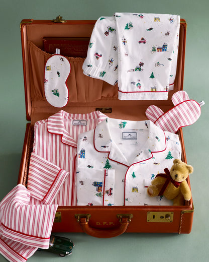 Children's pajama set with teddy bear and accessories in an open suitcase on a green background