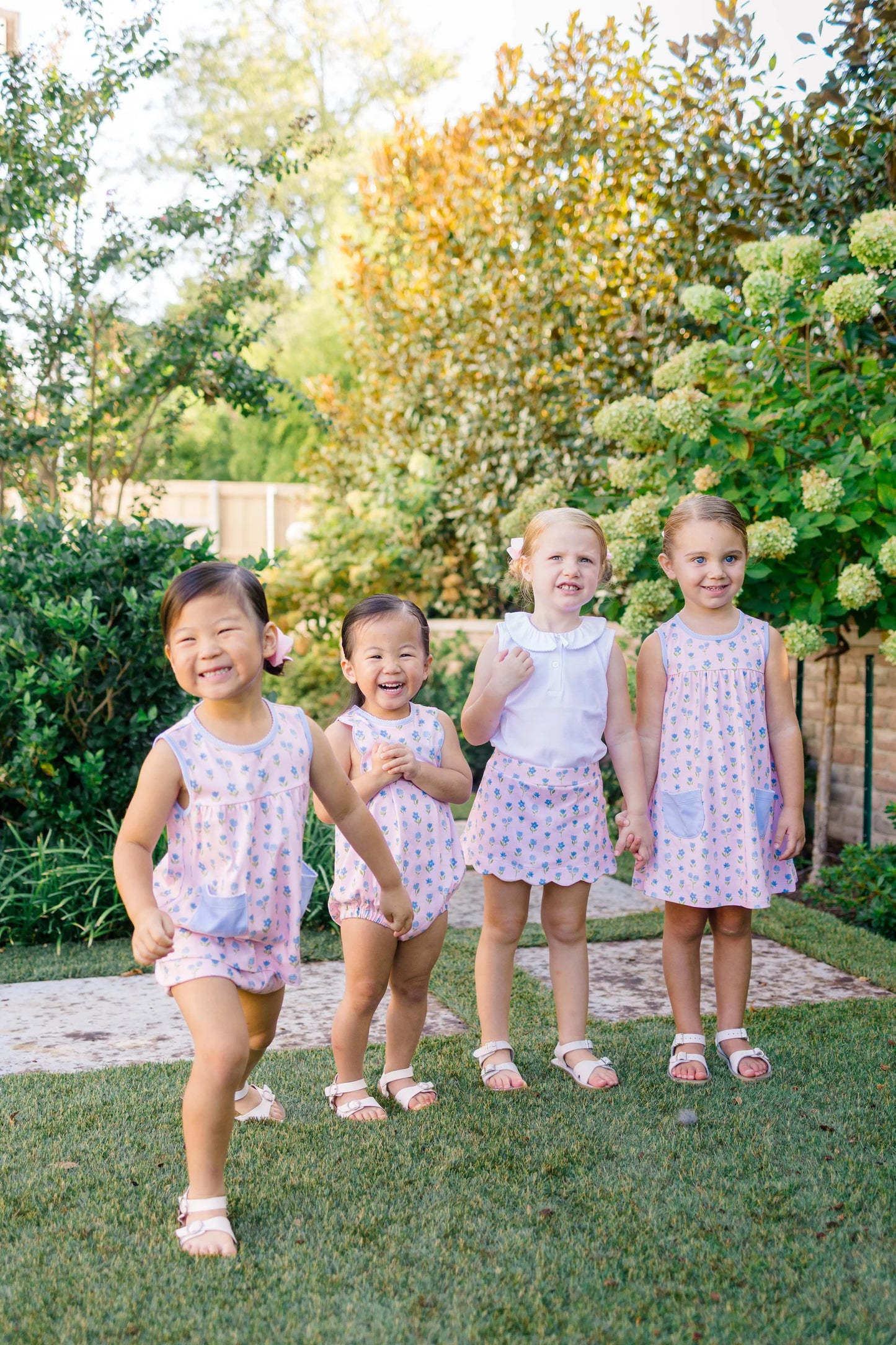 Four young girls in matching dresses standing on grass with trees in the background