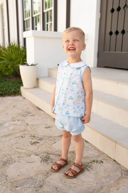 Young boy in light clothing standing on stone steps outside a house.