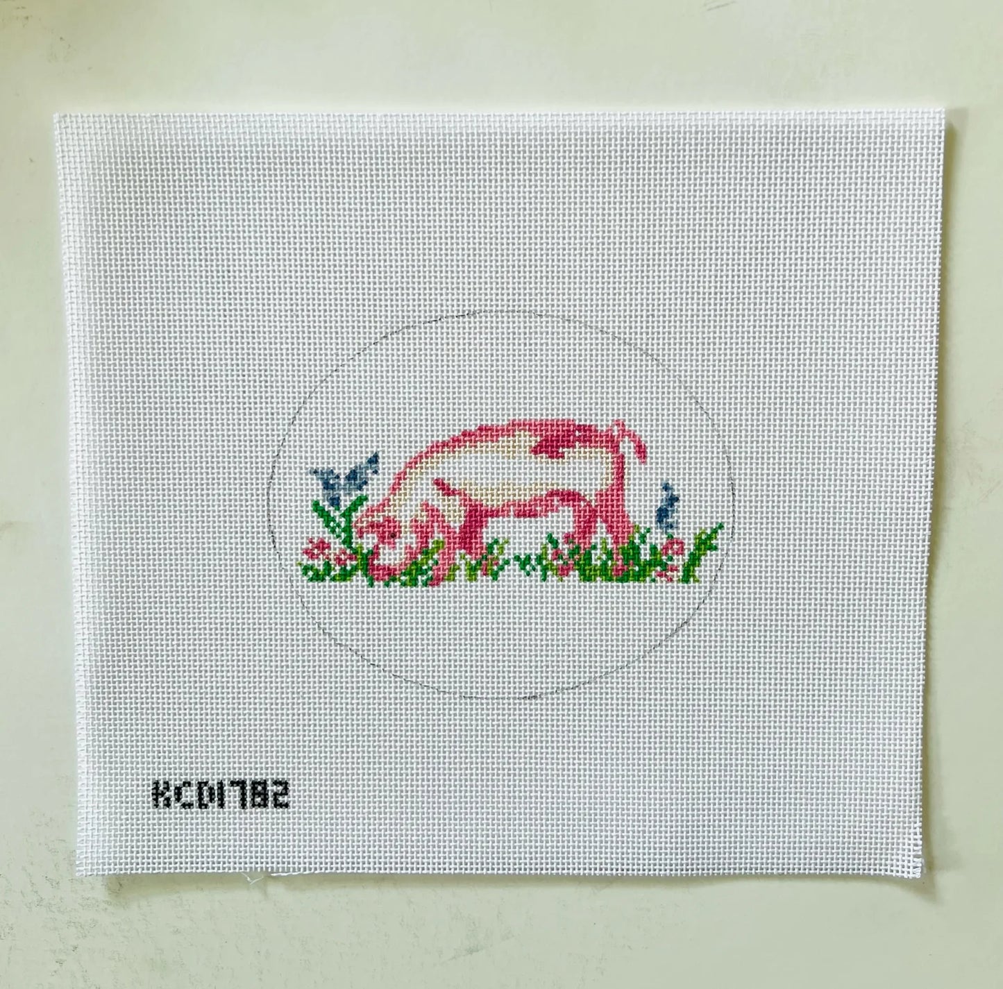 Cross-stitched design of a pig on a white fabric canvas with a circular border.