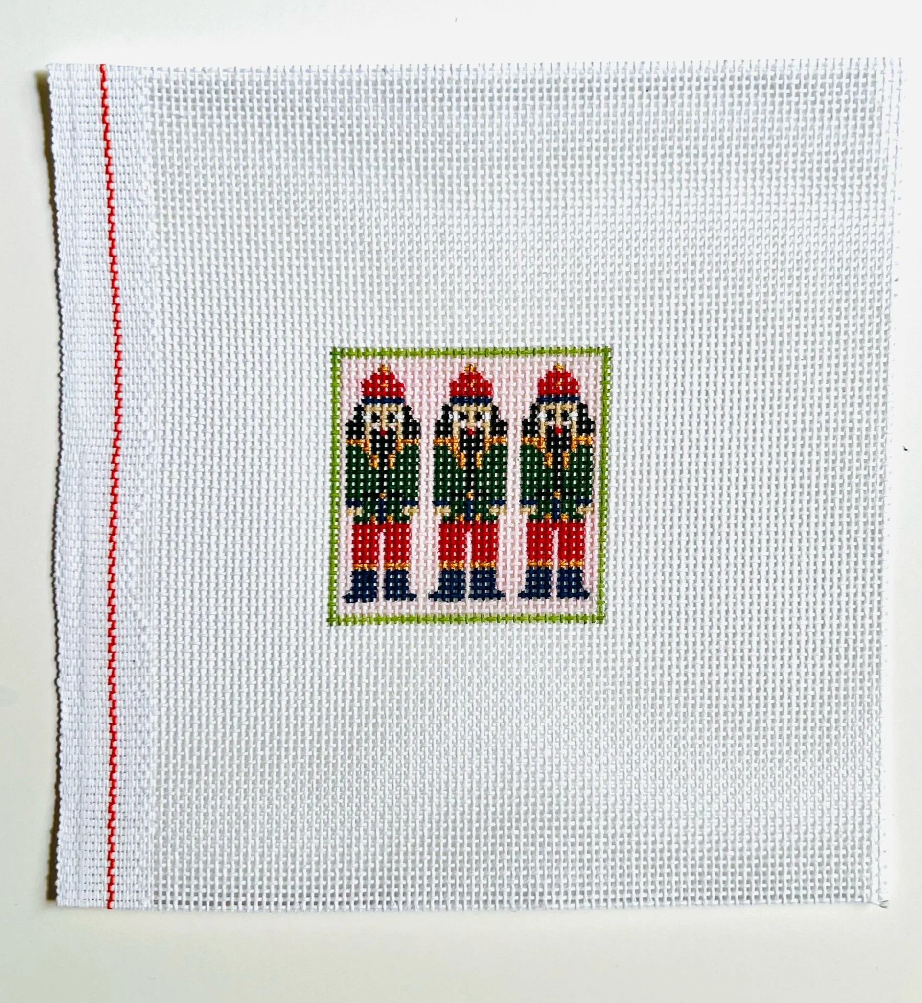 Cross-stitched design of three nutcrackers on a white fabric background