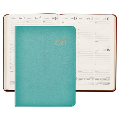 A 2027 daily planner with a textured blue cover and gold foil '2027' lettering, shown in front of an open view of the same planner displaying its daily and weekly layouts.
