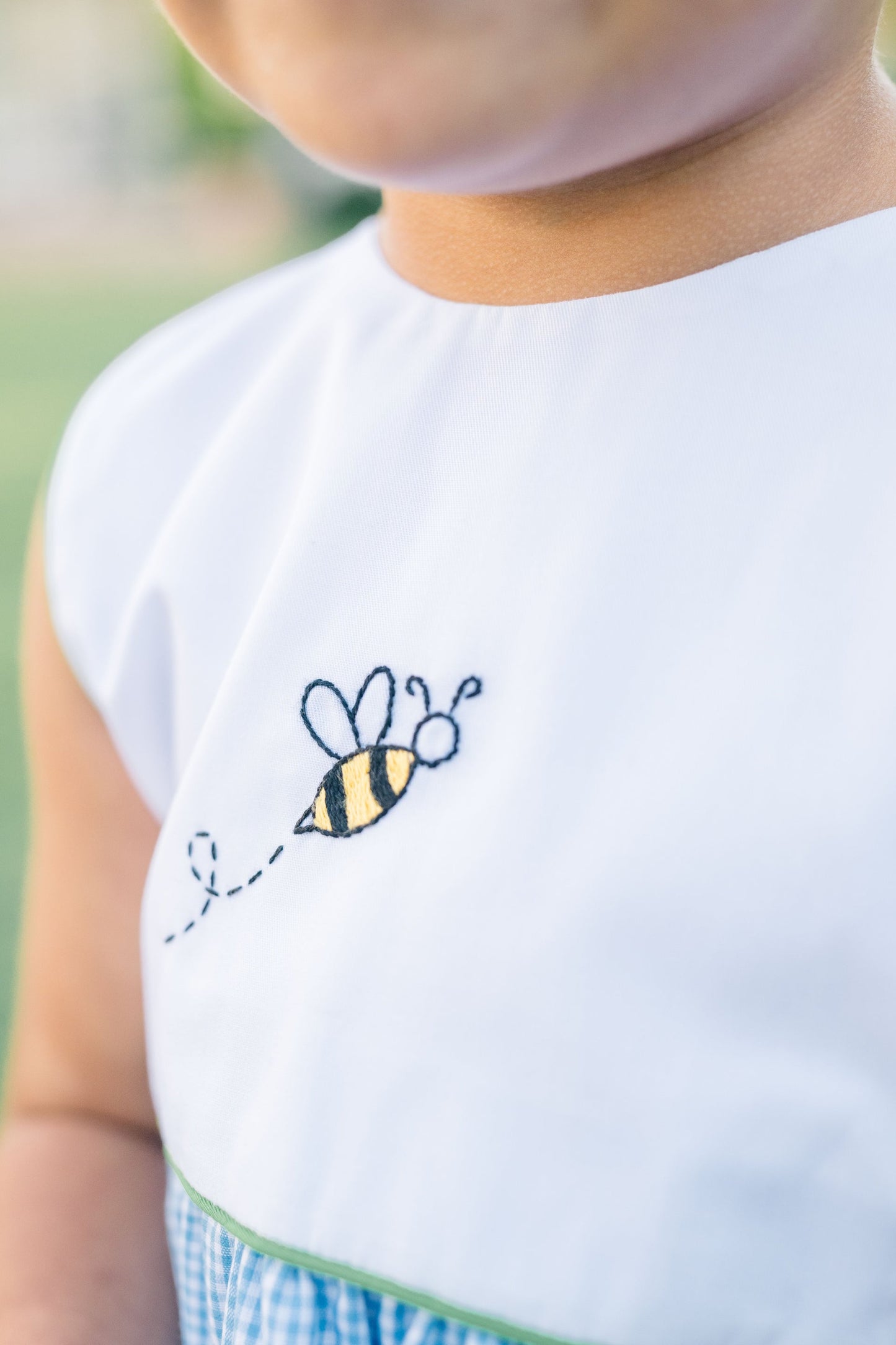 Child wearing a white shirt with a bee design on a blurred green background