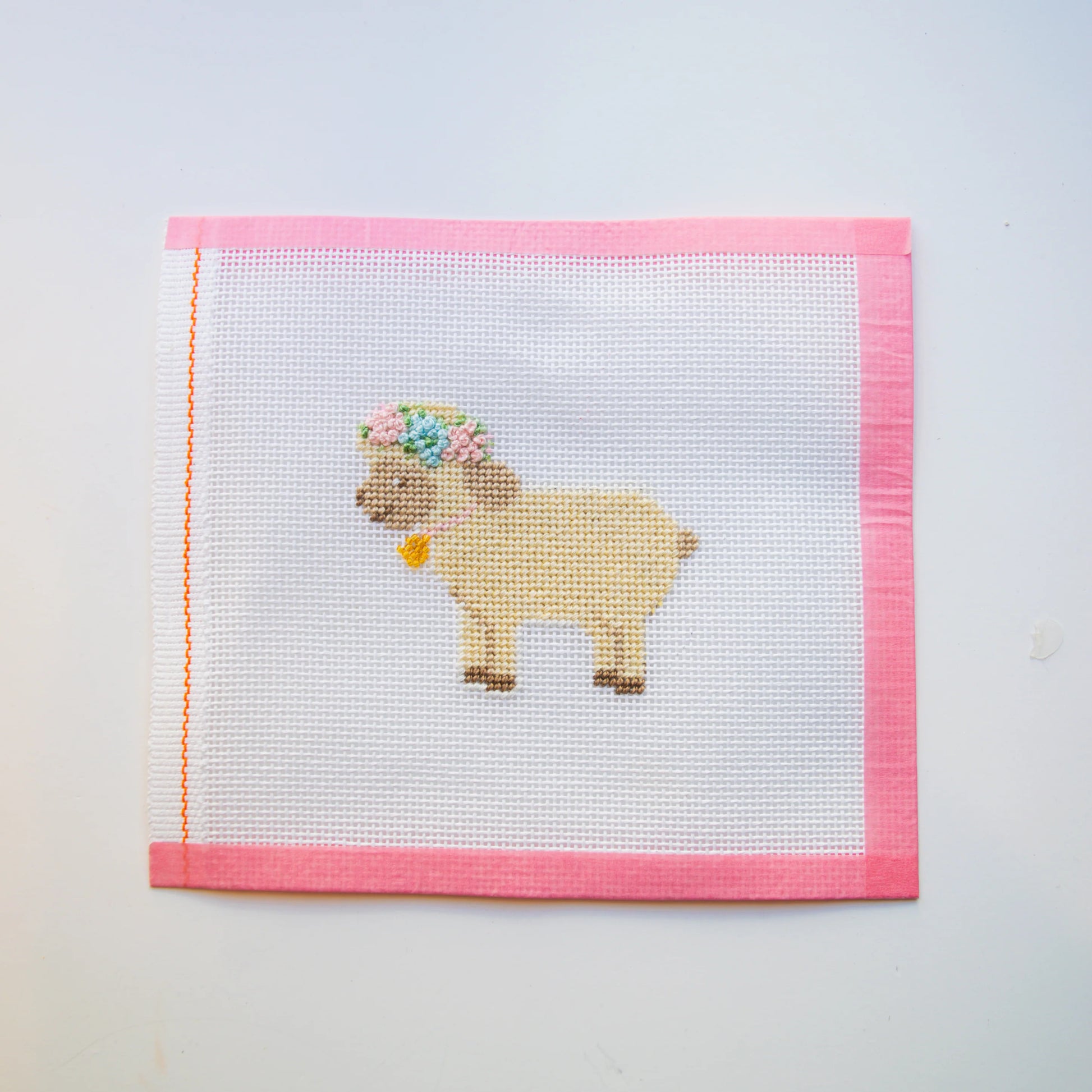 Cross-stitched design of a bear with flowers on a white fabric with pink border