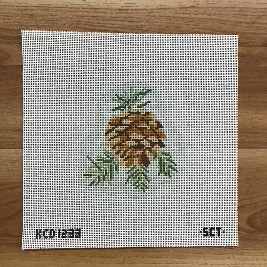 Cross-stitched pineapple design on a fabric canvas with 'SCT' branding, on a wooden surface.