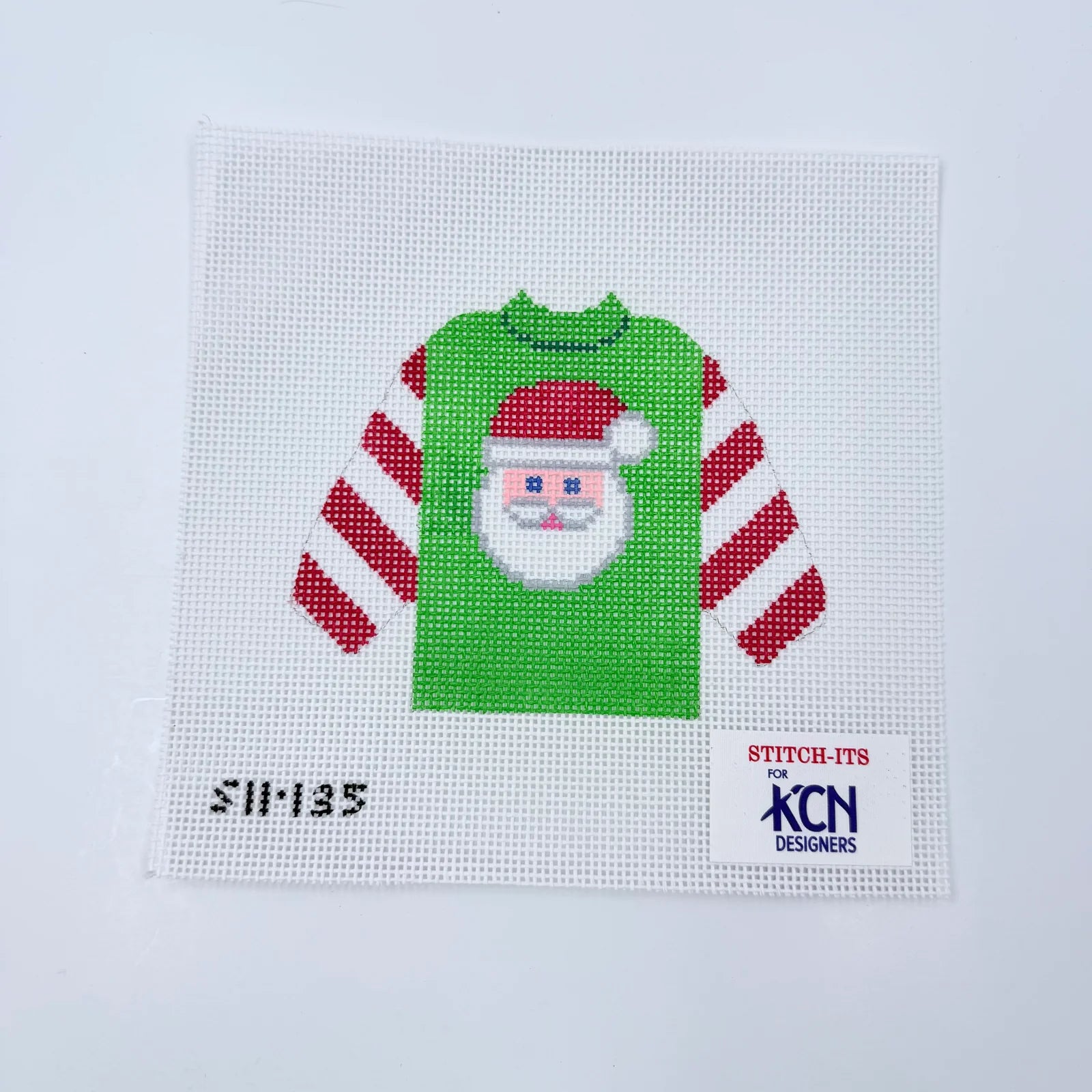 Cross-stitched design of a green shirt with a Santa Claus face on a white background, featuring 'Stitch-Its' and 'KCN Designers' logos.