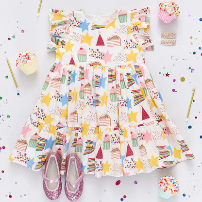 Colorful children's dress with cake and star patterns on a white background with confetti.