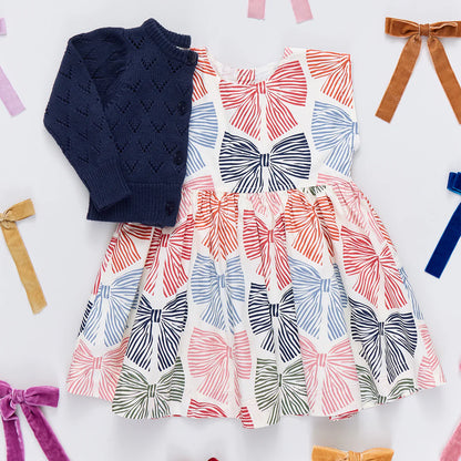 Dress with bow pattern and navy cardigan on a white background with colorful ribbons.