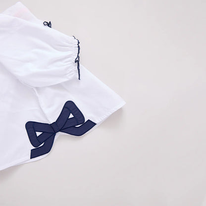 White shorts with a navy blue bow detail on a light gray background