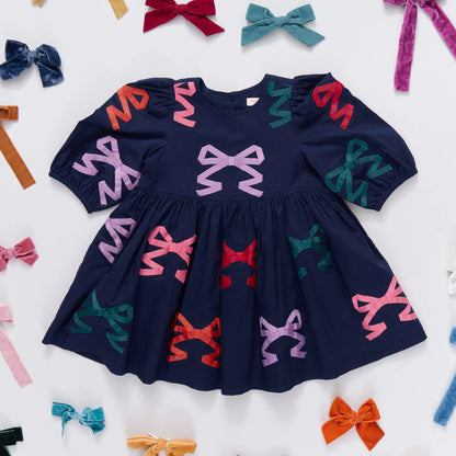 Navy blue dress with colorful bow patterns on a white background with scattered bows.