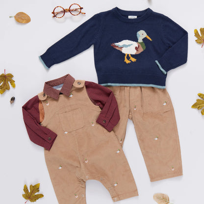 Children's clothing set with navy sweater with duck design and brown overalls on a white background.