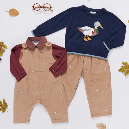 Children's navy sweater with duck design and beige overalls on a white background