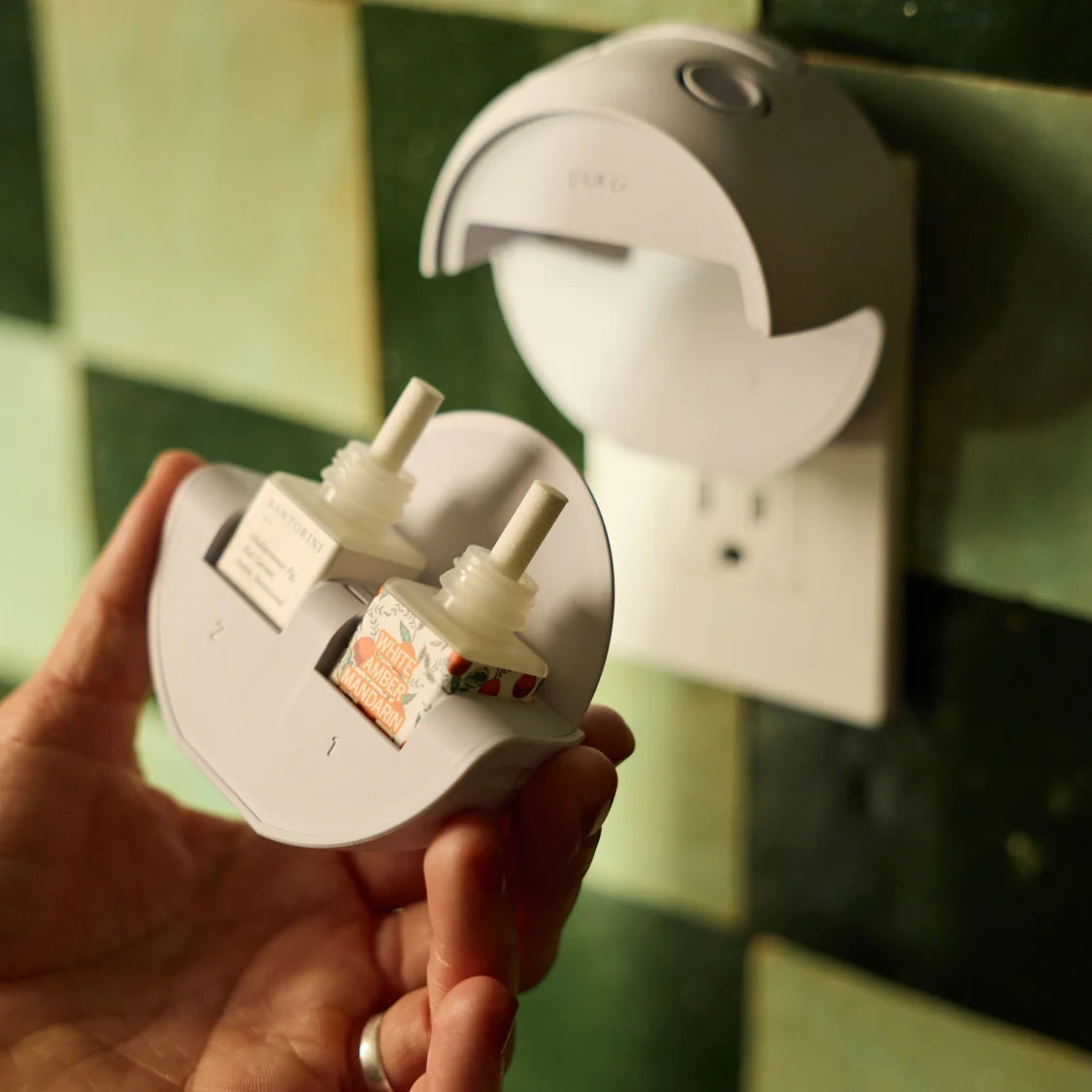 Hand holding a white electrical plug with a wall socket in the background
