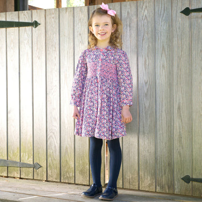 Young girl in a floral dress standing in front of a wooden gate.