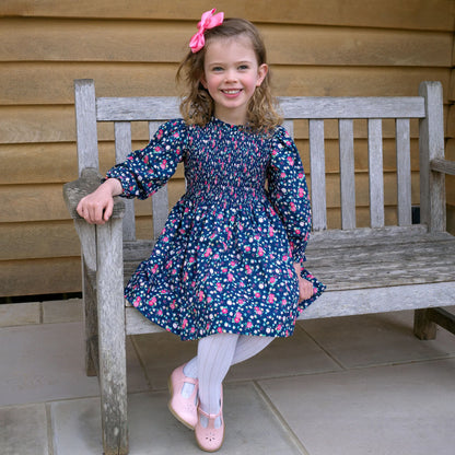 Young girl in a floral dress sitting on a wooden bench outdoors.