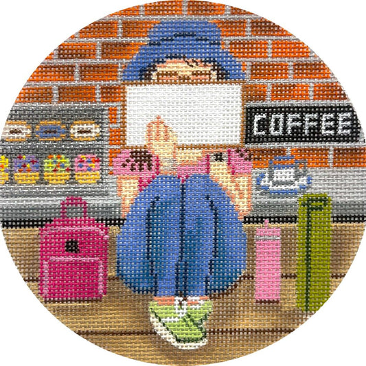 Circular needlepoint canvas with a person sitting at a coffee shop counter, surrounded by colorful elements.