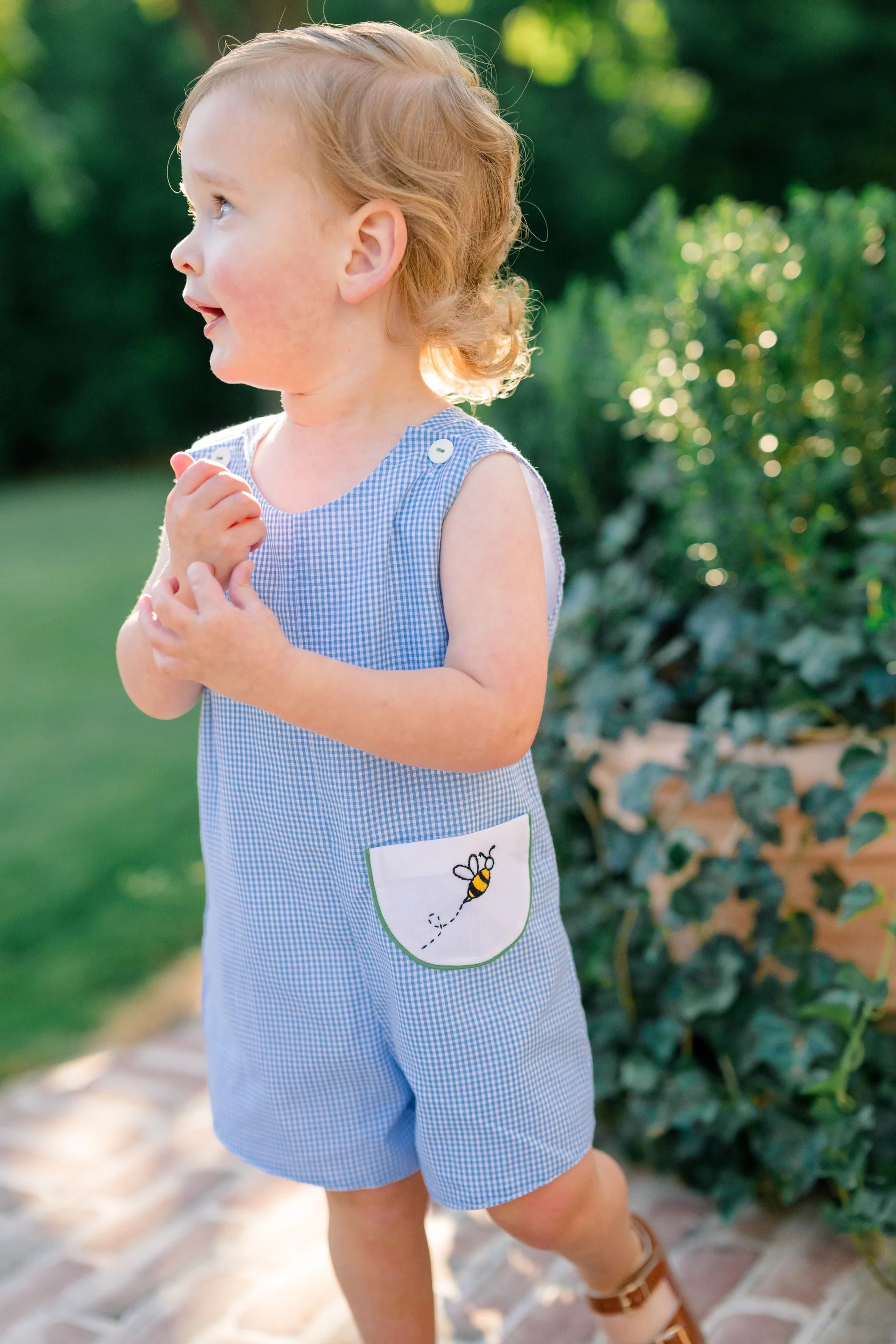 Child wearing a blue checkered romper with a pocket design outdoors.