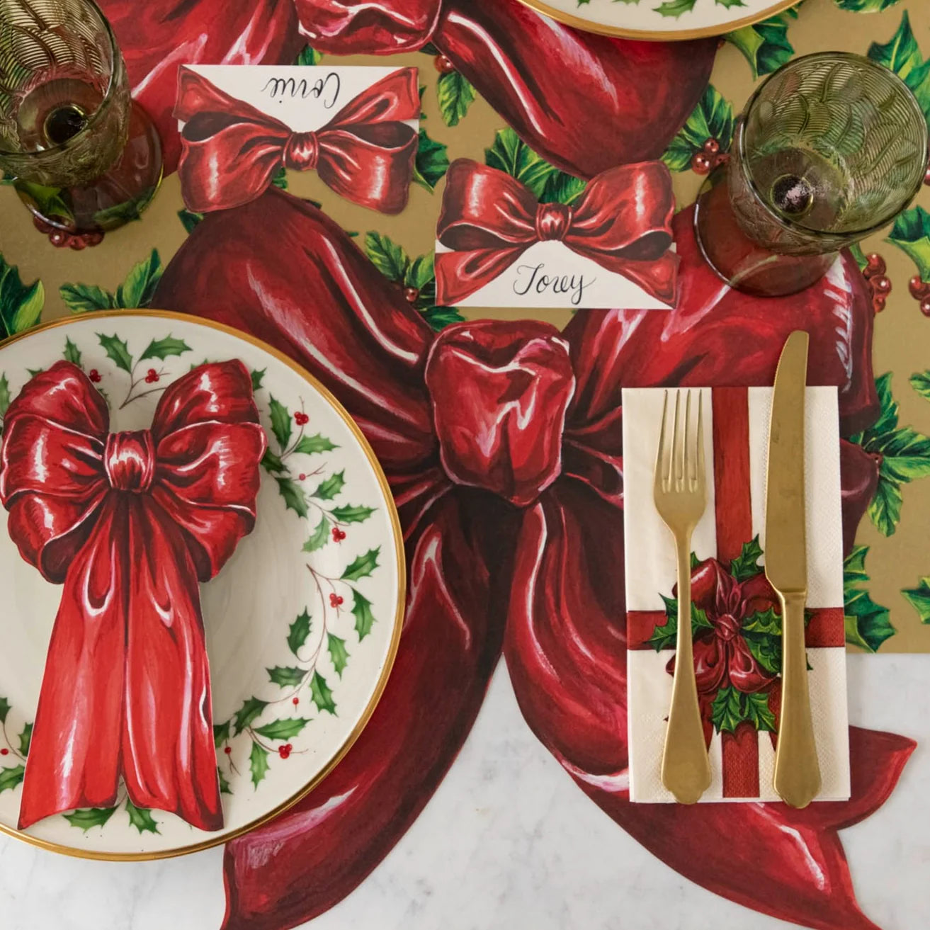 Christmas-themed table setting with red bows, holly leaves, and gold cutlery.