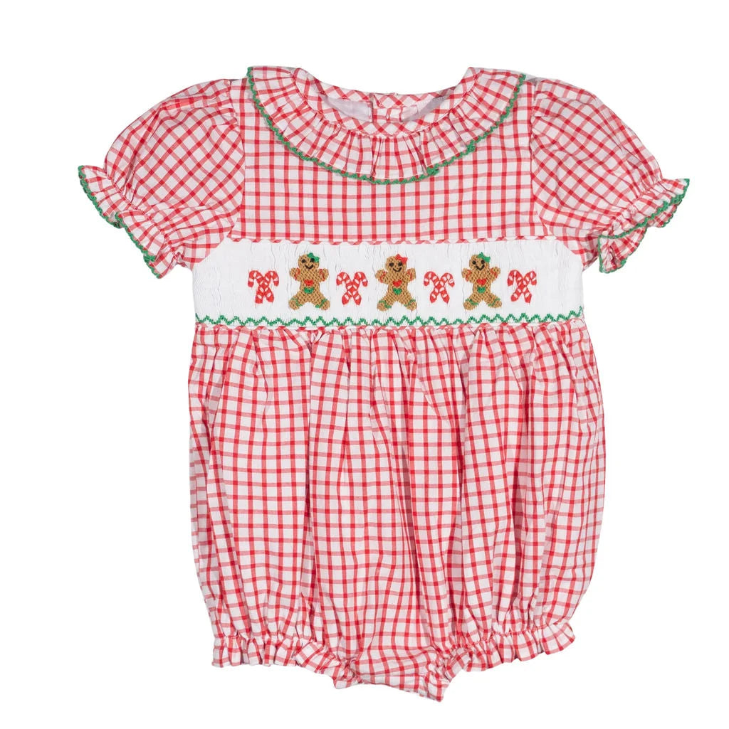 A baby girl's red and white gingham smocked romper with green trim and a white smocked band featuring gingerbread men and candy canes.