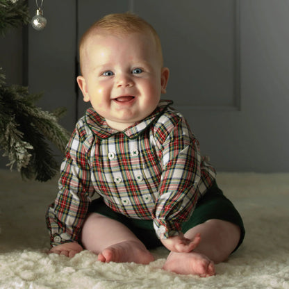 Baby wearing a plaid shirt sitting on a soft surface with a dark background