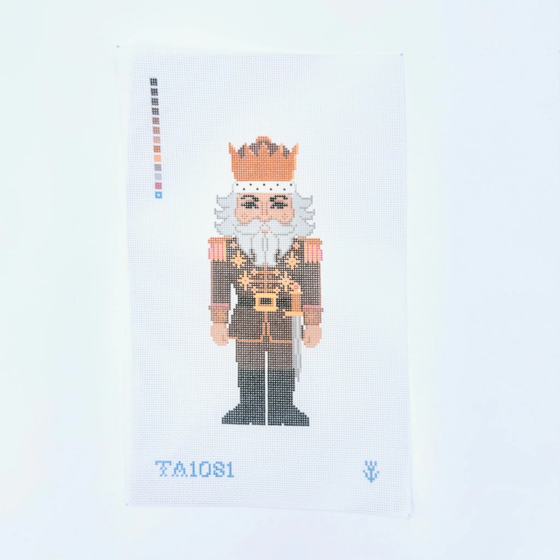 A needlepoint canvas featuring a pixelated nutcracker king design, with a color palette strip on the left and the text 'TA1081' at the bottom, set against a plain white background.