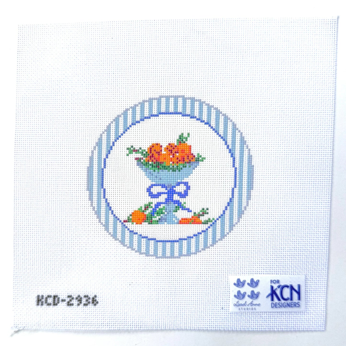 Cross-stitch pattern with a blue bowl and fruit design on white fabric, featuring KCN Designers logo.