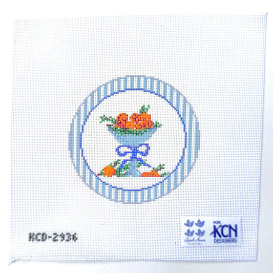 Cross-stitch pattern with a blue bowl and fruit design on white fabric, featuring KCN Designers logo.