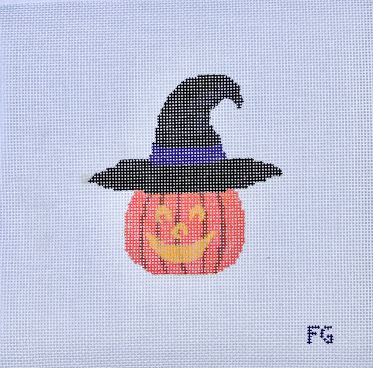 A needlepoint canvas featuring a pixelated design of a jack-o'-lantern pumpkin wearing a black witch hat with a purple band, on a white mesh grid. The initials 'FG' are printed in the bottom right corner.