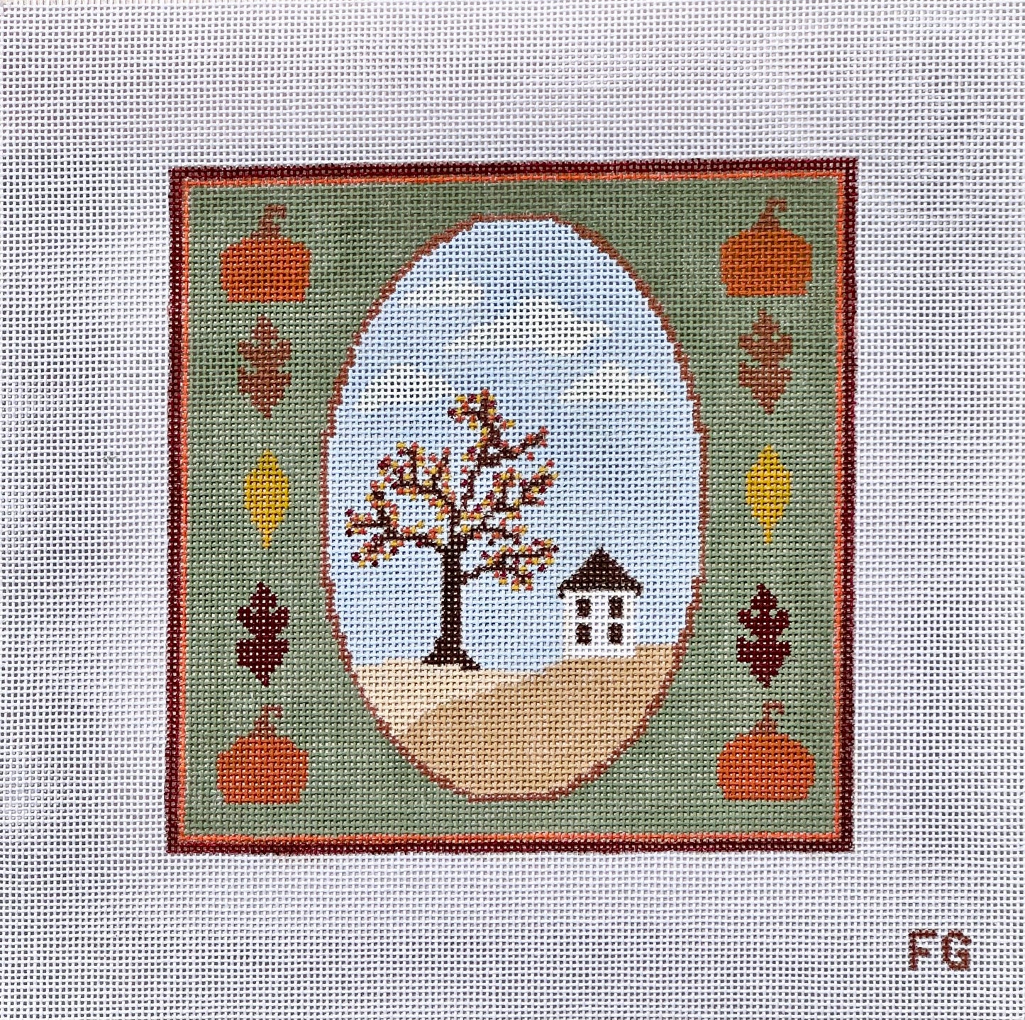 A square needlepoint canvas featuring a fall landscape design. The design has a green border with orange pumpkins, brown and yellow leaves, and a central oval showing a tree with brown and orange leaves, a small house, and a light blue sky.