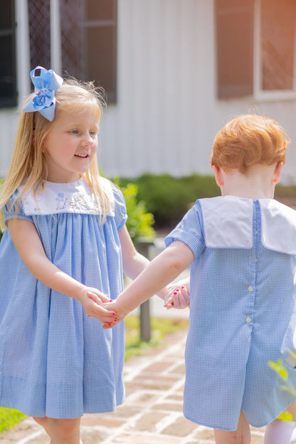 Two children in matching blue dresses standing on a path outdoors.