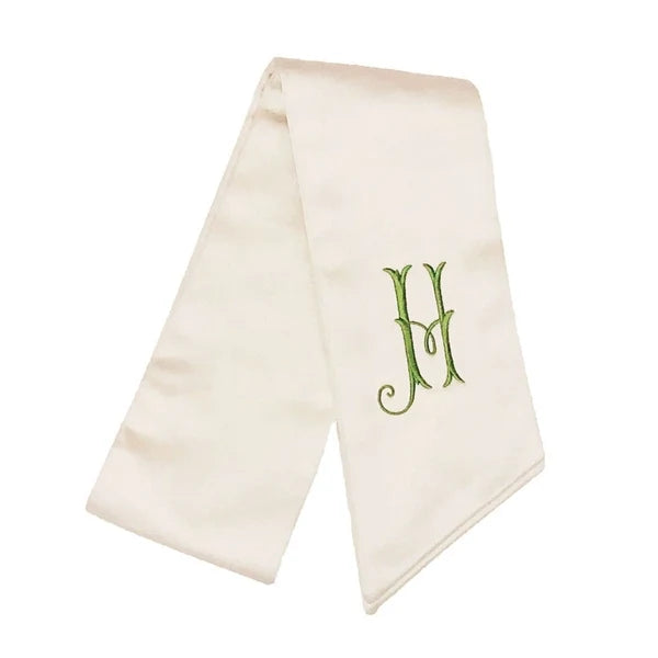 An ivory satin chalice veil with a green embroidered monogram letter 'H' on the front, displayed against a solid white background.