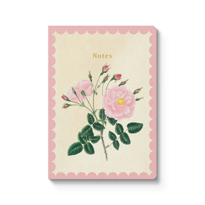 A vertical notebook or journal with a scalloped pink border, cream center, and a botanical illustration of pink roses and green leaves. The word 'Notes' appears near the top, and the item is photographed on a clean white background with a soft shadow.