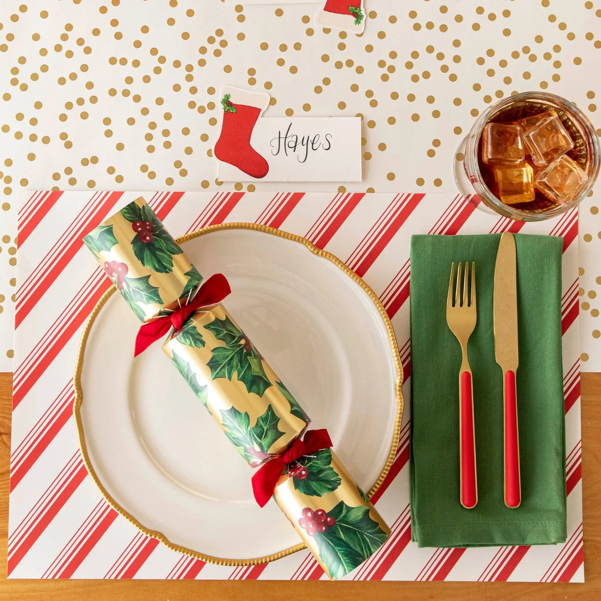 Christmas-themed table setting with a cracker, gold cutlery, and red and white striped placemat.