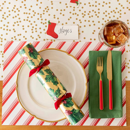 Christmas-themed table setting with a cracker, gold cutlery, and red and white striped placemat.