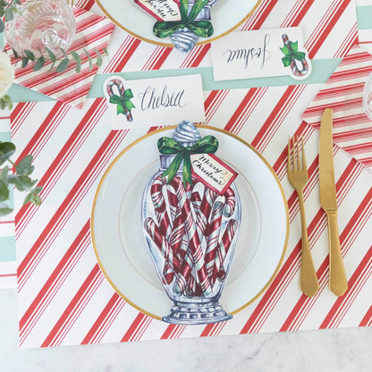 Christmas-themed table setting with candy canes, gold cutlery, and striped tablecloth.