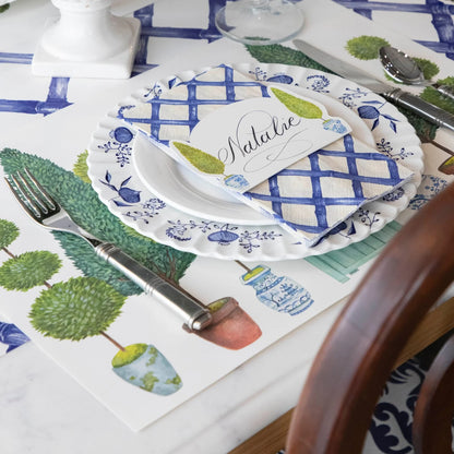 Table setting with blue and white checkered plates, green leafy patterns on placemats, and silverware.