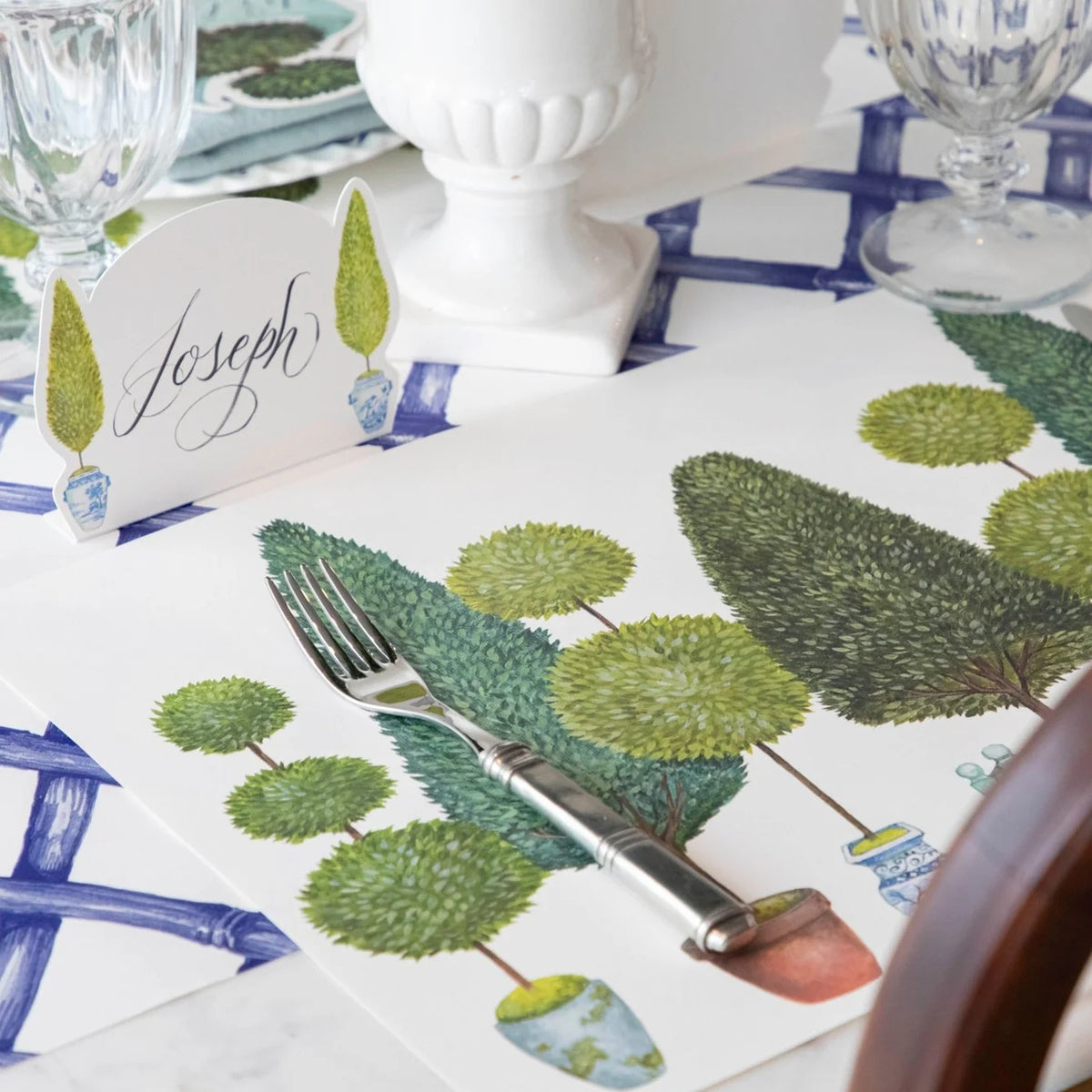 Table setting with decorative placemats featuring green leaf patterns, cutlery, and name cards.