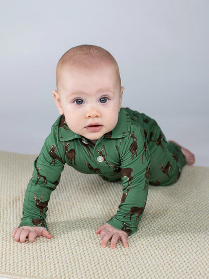 Baby in a green onesie with brown animal patterns on a light-colored surface.